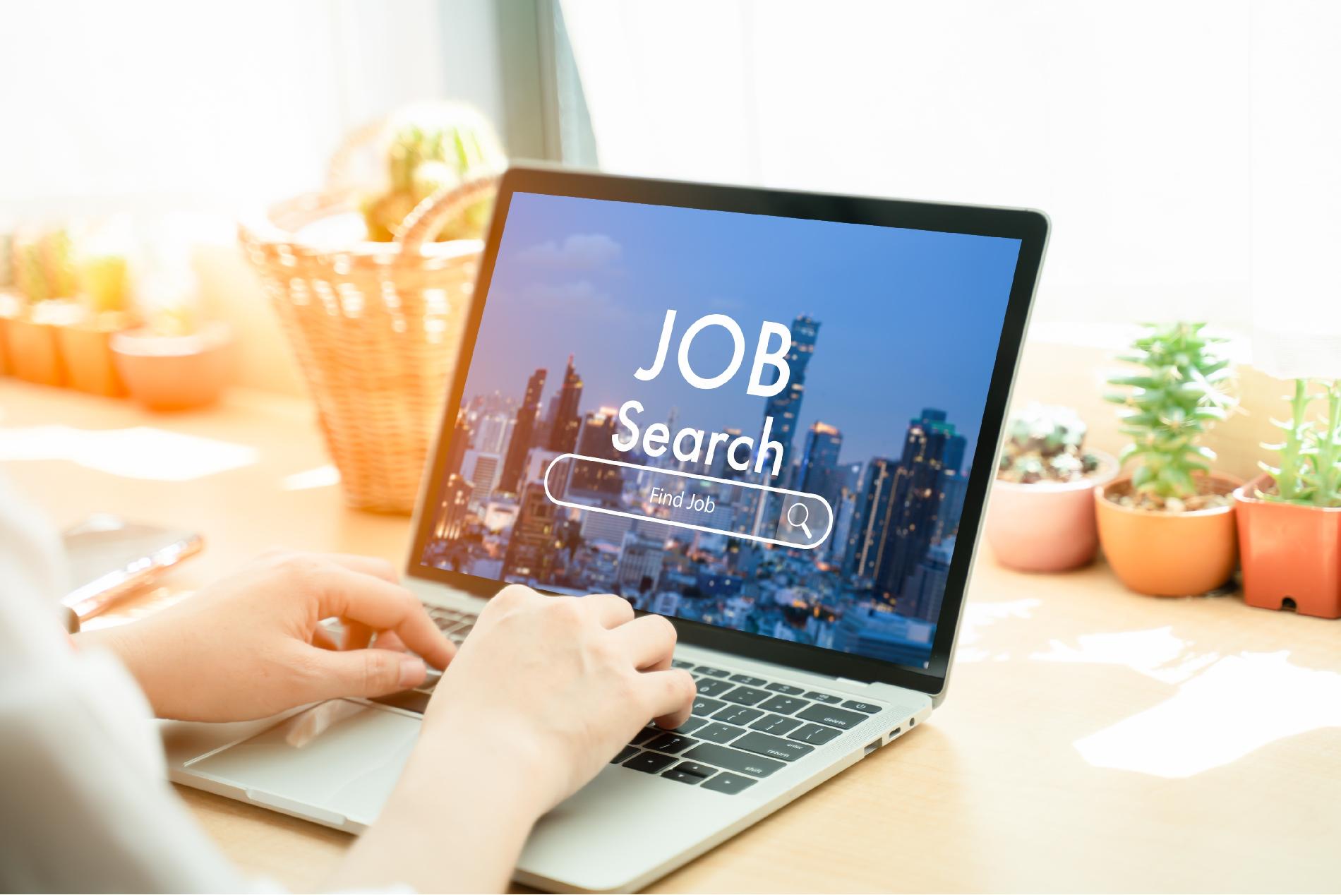 A graphic of a laptop on a desk with the a cityscape and the words Job Search and a search bar with the words find job across the screen