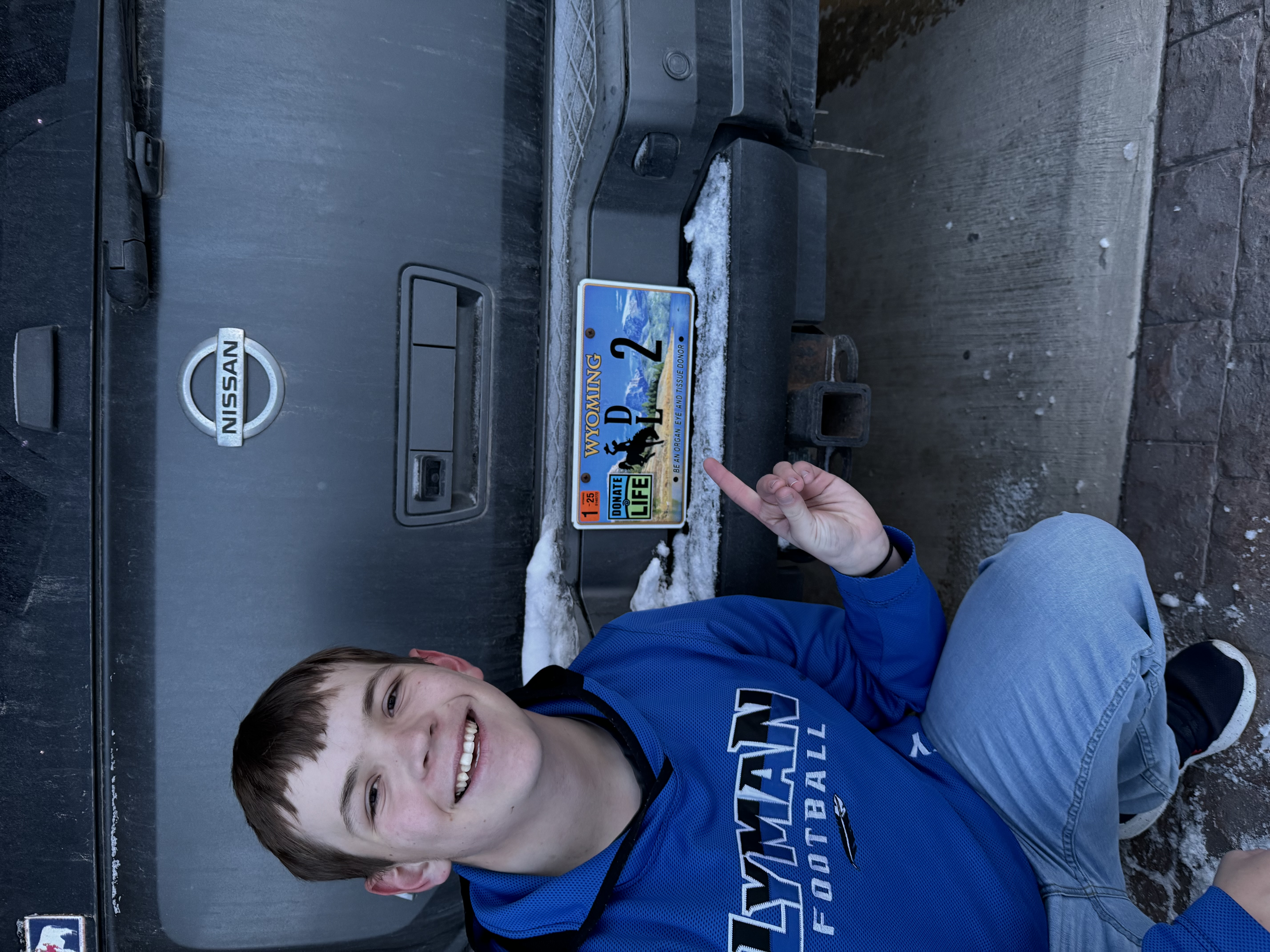 Bryson Quinney heart transplant recipient pointing to Donate Life Wyoming license plate number 2 on vehicle