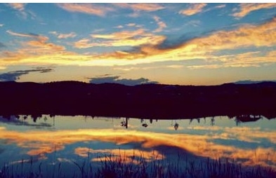 sunset with clouds reflected in small lake with reeds on shoreline